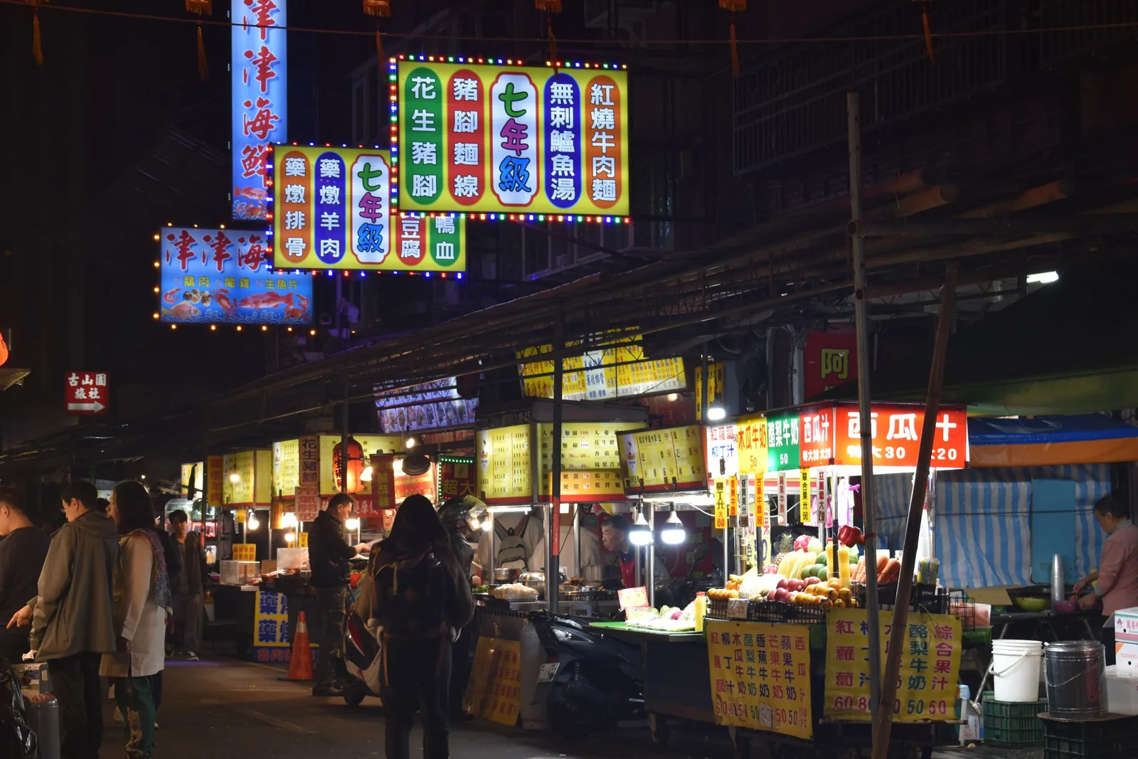夜晚街道兩側亮著招牌的小吃店與攤位，行人走過