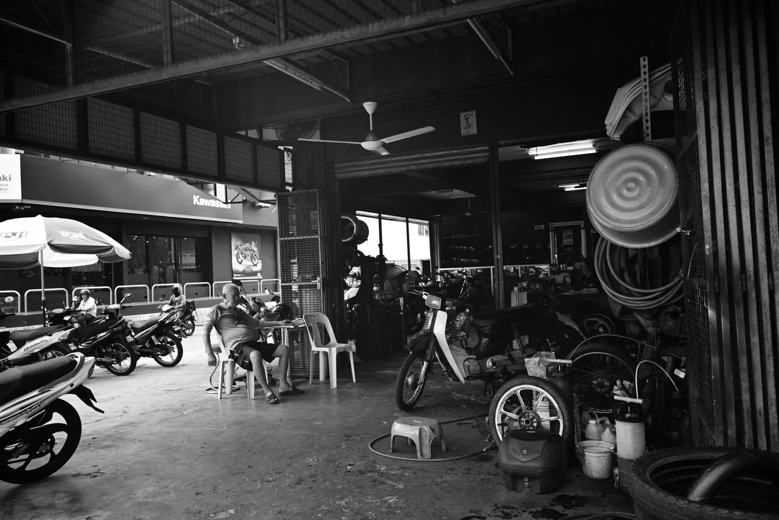 黑白照片：停滿機車與輪胎、工具的機車維修店