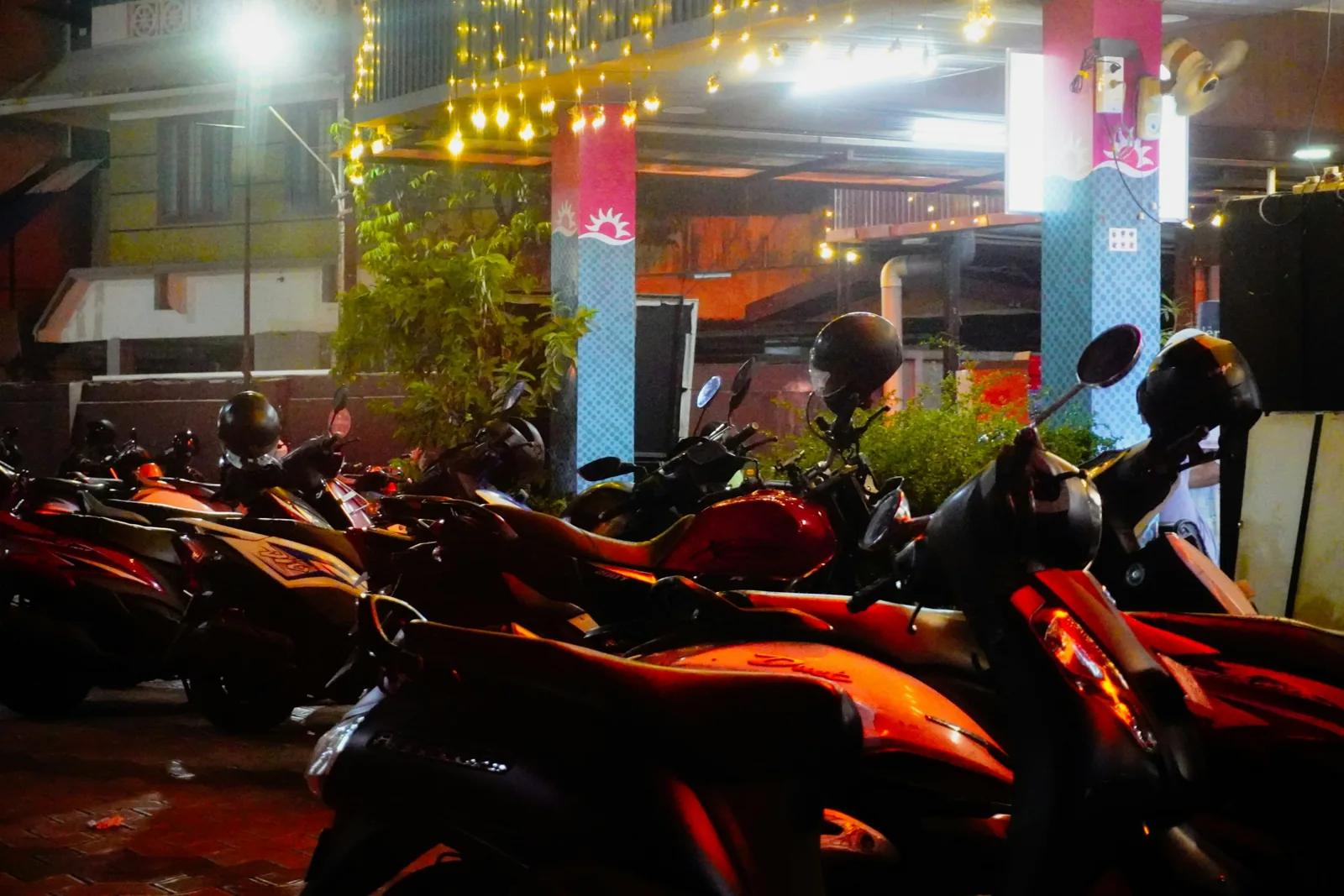 夜間燈光下並排停放的多輛機車，後照鏡上掛著安全帽